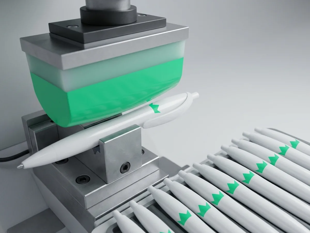 Máquina de tampografia imprimindo a marca no corpo curvo de canetas de plástico