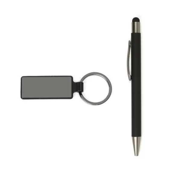 Caneta preta com ponteira touch e chaveiro retangular em metal ao lado de um notebook e de um vaso de planta sobre mesa branca