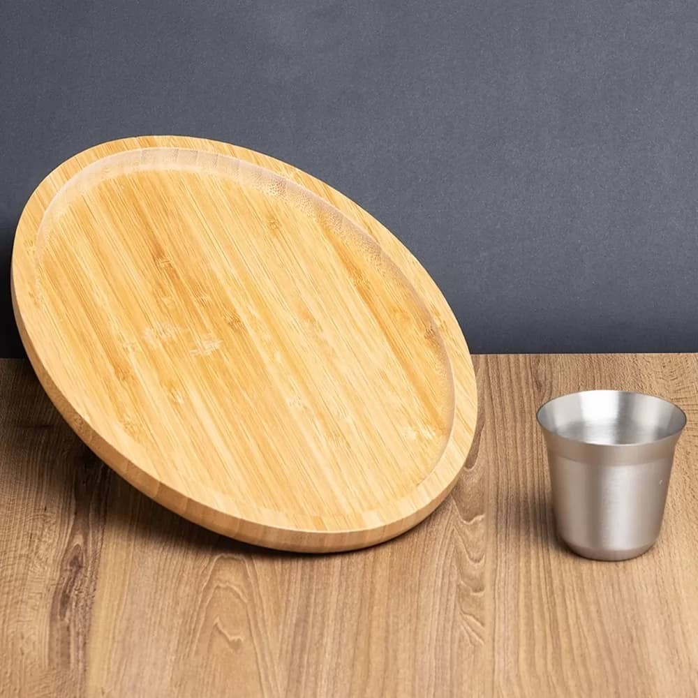 Kit aperitivo com tábua redonda de bambu inclinada e copo de inox sobre mesa de madeira
