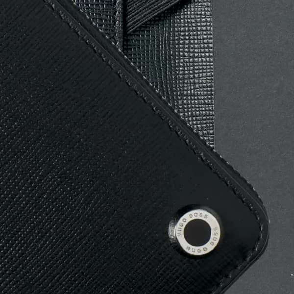 Detalhe da pasta executiva preta com acabamento texturizado e emblema metálico Hugo Boss