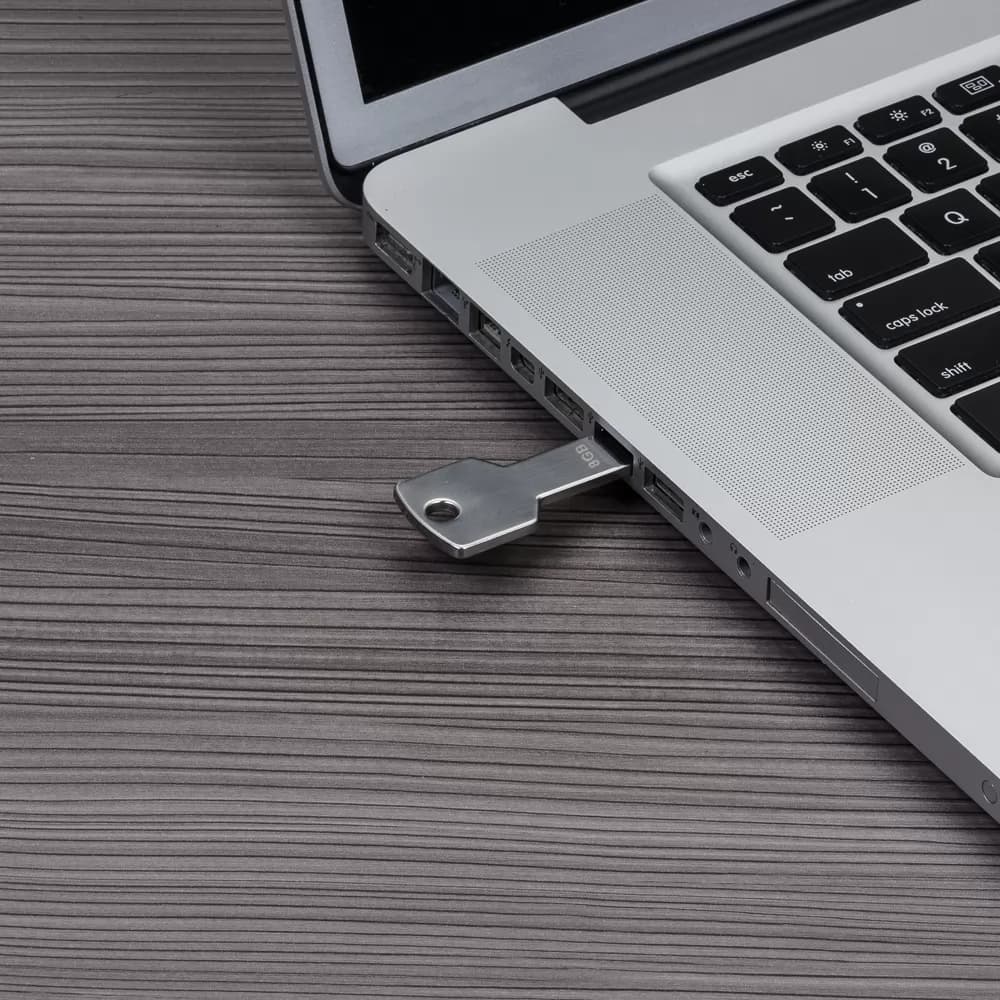 Pen drive chave prata metálico de 8GB conectado na porta USB lateral de um notebook