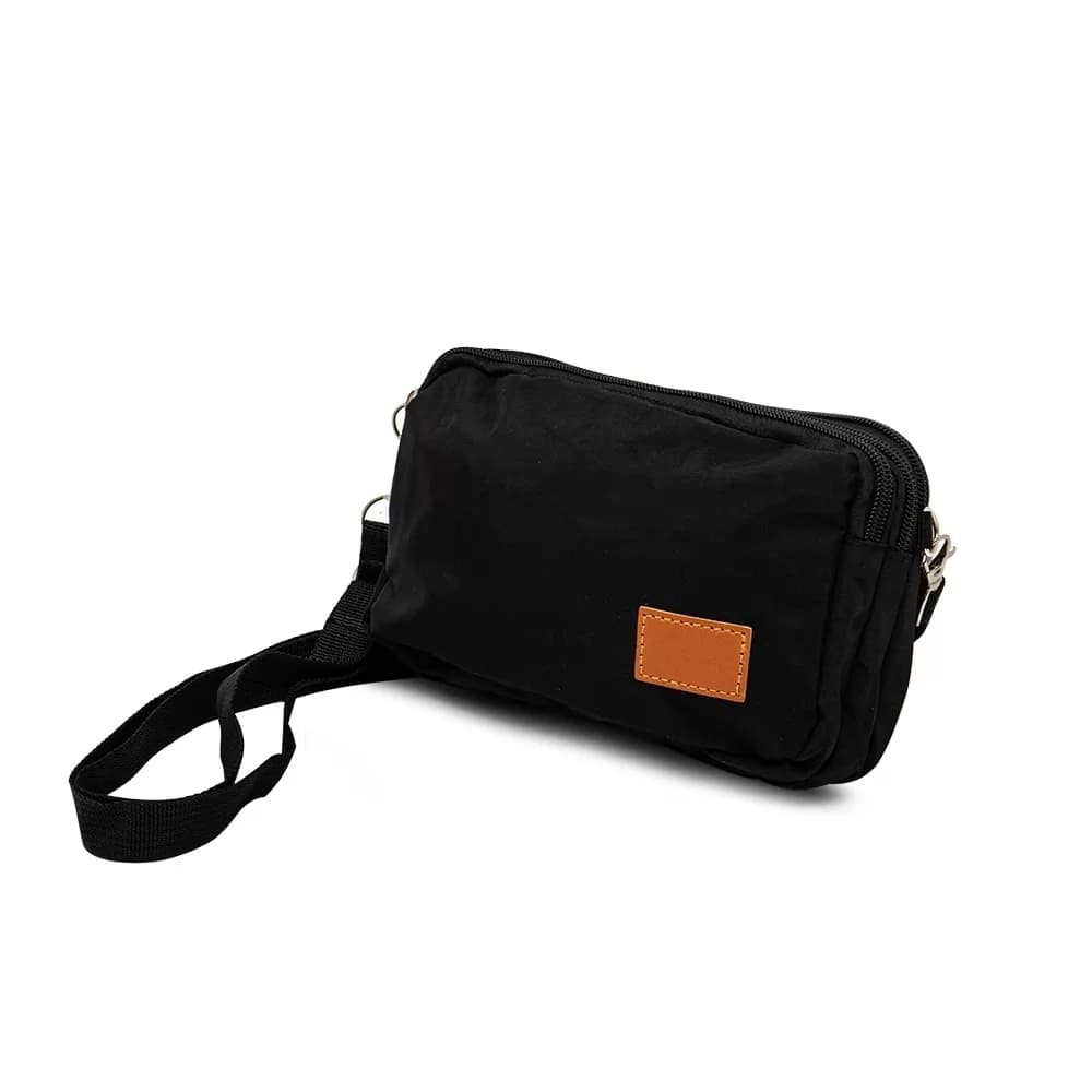 Mini bolsa transversal preta de nylon vista em ângulo, com alça e etiqueta retangular marrom na frente.